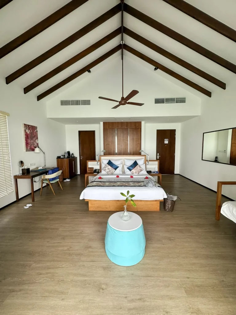 Weitwinkelaufnahme des hellen Innenraums einer Water Villa mit Holzdecke, Doppelbett und Holzboden im Robinson Club NOONU
